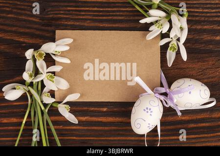 Tradizionale sfondo pasquale con copyspace. Fiori di neve e uova di pasqua con etichetta vuota su un tavolo in legno marrone Foto Stock