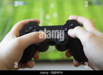 Uomo che gioca a calcio in TV. Controller gamepad in mano Foto Stock