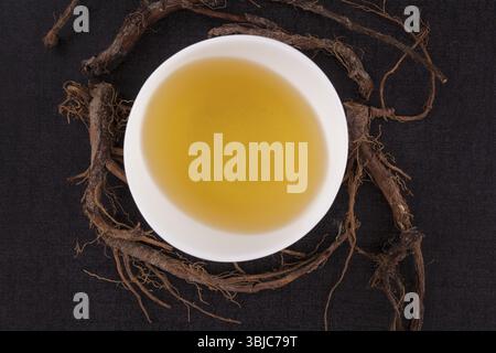 Tè al dente di leone e radici di dente di leone, isolate dall'alto su sfondo nero. Medicina alternativa, rimedio naturale Foto Stock