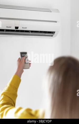 Donna che tiene il telecomando rivolto al condizionatore d'aria Foto Stock