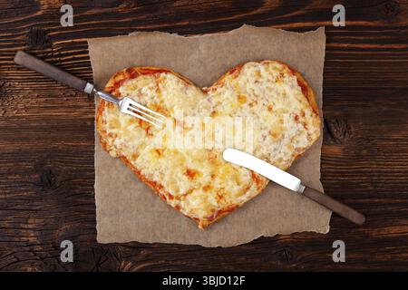 Deliziosa pizza a forma di cuore su un tavolo in legno, vista dall'alto. Cucina a base di pizza. Amo la pizza Foto Stock