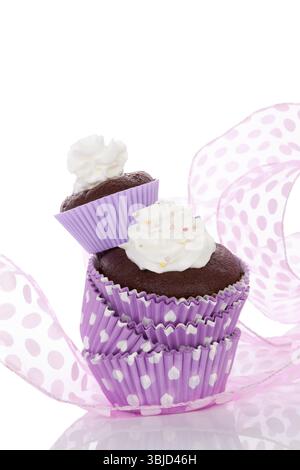 Delizioso cupcake al cioccolato con panna montata in carta punteggiata viola isolata su bianco. Cottura dei cupcake Foto Stock