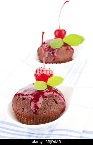 Deliziosi muffin al cioccolato decorati con marmellata, ciliegia e foglie di menta fresca su un panno da cucina. Cibo dolce Foto Stock