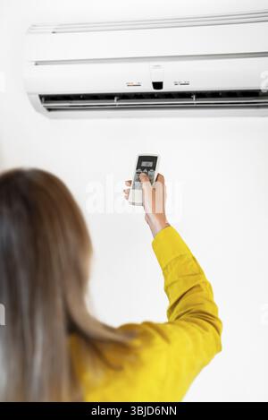 Donna che tiene il telecomando rivolto al condizionatore d'aria Foto Stock