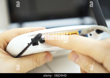 Uomo che preme il pulsante di accensione sul router wifi Foto Stock