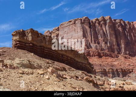 Alte formazioni rocciose a strati si innalzano drammaticamente contro un cielo blu profondo in un'area desertica remota. La luce del sole mette in risalto le texture e i colori del ro Foto Stock