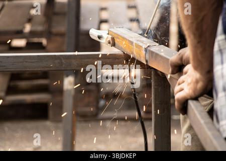 Saldatura di parti metalliche con scintille e fumo - il processo di lavoro di una saldatrice che unisce elementi metallici con saldatura manuale Foto Stock