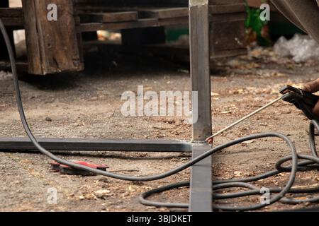 Saldatura di parti metalliche con scintille e fumo - il processo di lavoro di una saldatrice che unisce elementi metallici con saldatura manuale Foto Stock
