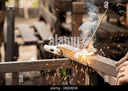 Saldatura di parti metalliche con scintille e fumo - il processo di lavoro di una saldatrice che unisce elementi metallici con saldatura manuale Foto Stock