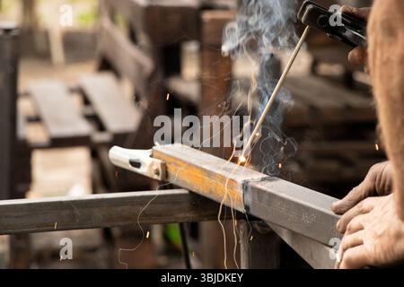 Saldatura di parti metalliche con scintille e fumo - il processo di lavoro di una saldatrice che unisce elementi metallici con saldatura manuale Foto Stock