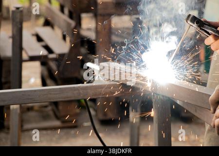 Saldatura di parti metalliche con scintille e fumo - il processo di lavoro di una saldatrice che unisce elementi metallici con saldatura manuale Foto Stock