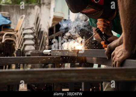 Saldatura di parti metalliche con scintille e fumo - il processo di lavoro di una saldatrice che unisce elementi metallici con saldatura manuale Foto Stock