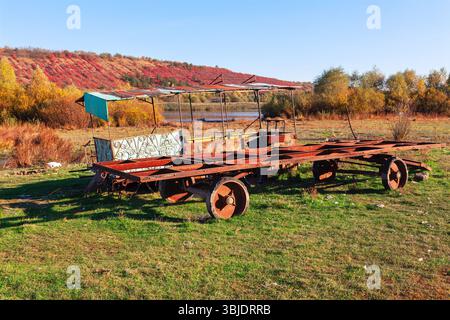 Il trasporto di metallo abbandonato si trova su un campo erboso accanto a un fiume. Veicolo di trasporto resistente agli agenti atmosferici, il suo telaio mostra il passare del tempo Foto Stock