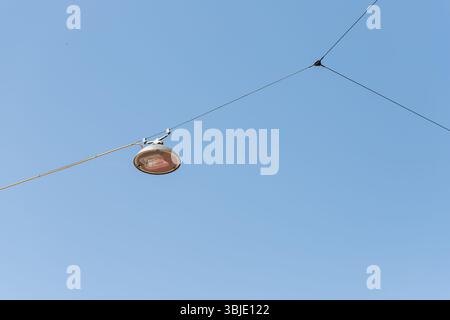 Ripresa ad angolo basso di un lampione sospeso da cavi contro un cielo azzurro. Foto Stock