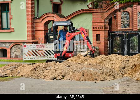 10 giugno 2025 - Teschendorf, Germania: Mini escavatore per la preparazione della trincea per l'installazione di cavi in fibra ottica, parte dell'infrastruttura rurale tedesca Foto Stock