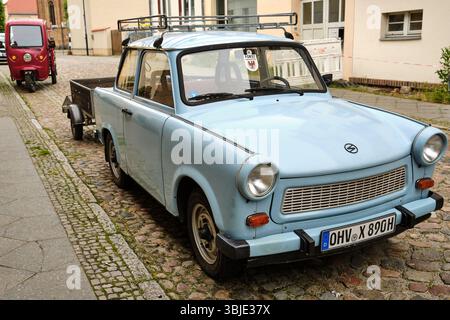 10 giugno 2025 - Fürstenberg-Germania: Trabant azzurro con rimorchio parcheggiato in strada acciottolata nella storica città tedesca orientale di Fürstenberg, Nor Foto Stock