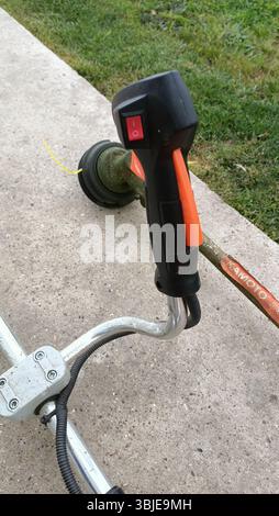 Questa immagine mostra un primo piano di un'impugnatura e di una testa di taglio elettrici per taglierine su una superficie in cemento Foto Stock
