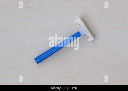 Vista dall'alto di un rasoio blu con lame affilate, isolato su legno chiaro. Concetto di rasatura e igiene. Foto Stock