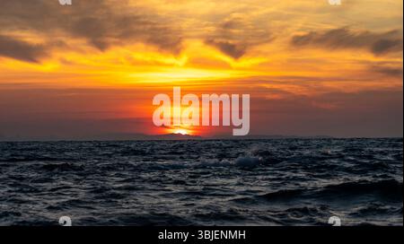 Un tramonto mozzafiato sull'oceano, con vivaci sfumature arancioni e gialle che si fondono nel cielo. Le onde ondulano delicatamente in primo piano, riflettendo il Foto Stock