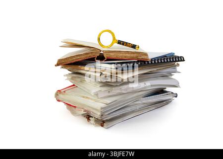 Libro vintage aperto e una lente d'ingrandimento sopra un'alta pila di cartelle e documenti, isolata sul bianco Foto Stock