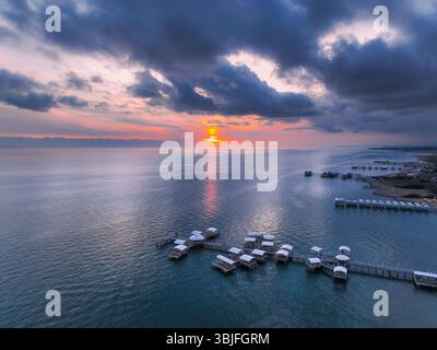 Splendida vista aerea del lago Issyk Kul al tramonto, caratterizzato da un cielo spettacolare con i raggi del sole che si riflettono sull'acqua e case galleggianti uniche sui moli Foto Stock