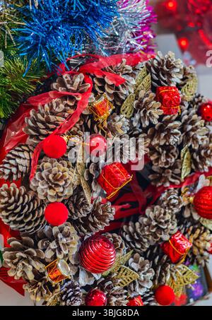 Primo piano di una corona di Natale fatta di coni di pino decorati con palle rosse, nastri e ornamenti lucenti, simbolo di spirito festivo e intimità Foto Stock