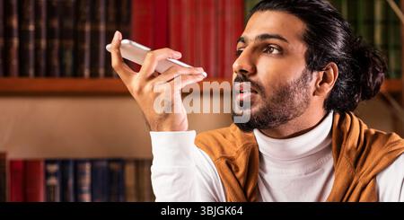 Studente indiano che usa Voice Assistant su smartphone seduto in casa Foto Stock