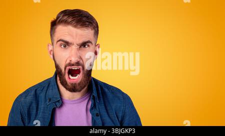Ritratto di giovane ragazzo bearded gridando furiosamente, esprimendo la sua rabbia su sfondo grigio studio. Emozioni negative Foto Stock