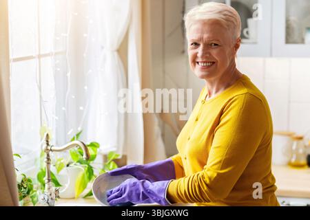 Allegra signora senior lavare i piatti in cucina, utilizzando guanti di gomma Foto Stock