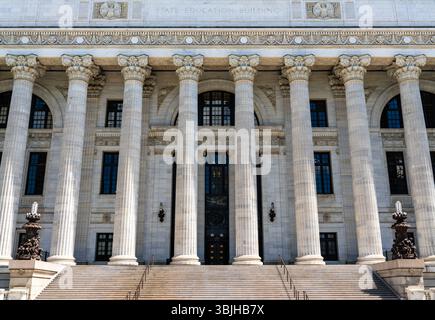 Imponenti colonne corinzie fiancheggiano la facciata in marmo del New York State Education Building ad Albany, Stati Uniti, le loro pietre bianche che brillano con il luminoso sole estivo sopra ampi gradini d'ingresso Foto Stock