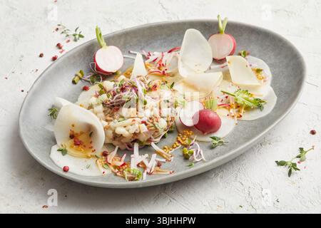 Tartare di noci di pera con kohlrabi su un piatto ovale grigio: Un antipasto o un antipasto leggero ed elegante a base di piante, perfetto per mangiare in modo pulito o per i menu estivi. Foto Stock