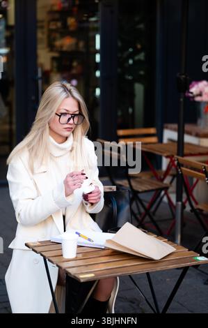 Nel mezzo della vibrante atmosfera del caffè all'aperto, una donna si gode la sua bevanda calda mentre è profondamente impegnata, disegnando idee su carta con calma concentrazione Foto Stock