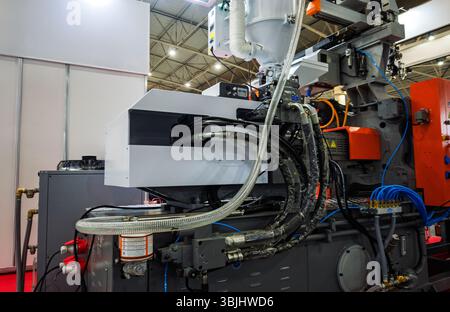 Dettaglio dettagliato di una macchina industriale per lo stampaggio a iniezione di plastica complessa che mostra una rete complessa di tubi flessibili, tubi e cablaggi in un settore di produzione o fa Foto Stock