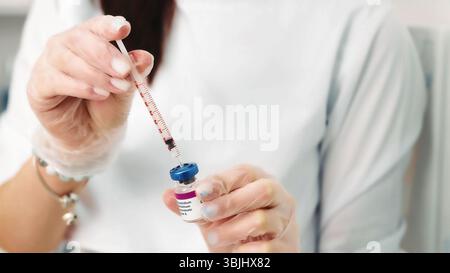 Primo piano della soluzione di prelievo della siringa dal flaconcino in ambiente medico. Immagine ravvicinata di mani con i guanti che aspirano con cura una soluzione in una siringa da a. Foto Stock