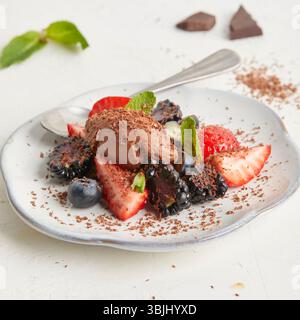 Mousse al cioccolato con fragole fresche, mirtilli e more su un piatto bianco: Un dessert ricco ma fresco, perfetto per l'estate. Foto Stock