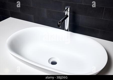 Dettagli interni del bagno con lavabo con lavabo a soffitto ovale e rubinetto. Bagno con lavandino interno con pareti piastrellate nere e moderne dimensioni piatte Foto Stock