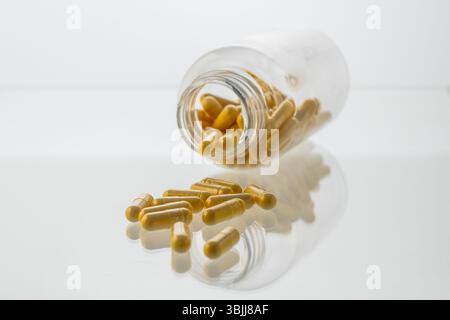 Un vaso con le pillole all'interno giace su uno sfondo bianco. Acido ialuronico, collagene, vitamine o mirtillo per perdere peso. Preparazioni mediche per la salute Foto Stock