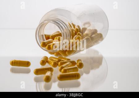 Un vaso con le pillole all'interno giace su uno sfondo bianco. Acido ialuronico, collagene, vitamine o mirtillo per perdere peso. Preparazioni mediche per la salute Foto Stock