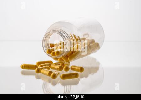 Un vaso con le pillole all'interno giace su uno sfondo bianco. Acido ialuronico, collagene, vitamine o mirtillo per perdere peso. Preparazioni mediche per la salute Foto Stock