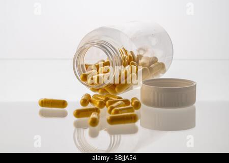 Un vaso con le pillole all'interno giace su uno sfondo bianco. Acido ialuronico, collagene, vitamine o mirtillo per perdere peso. Preparazioni mediche per la salute Foto Stock