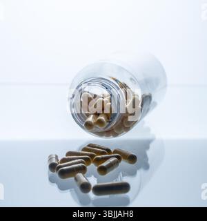Un vaso con le pillole all'interno giace su uno sfondo bianco. Acido ialuronico, collagene, vitamine o mirtillo per perdere peso. Preparazioni mediche per la salute Foto Stock