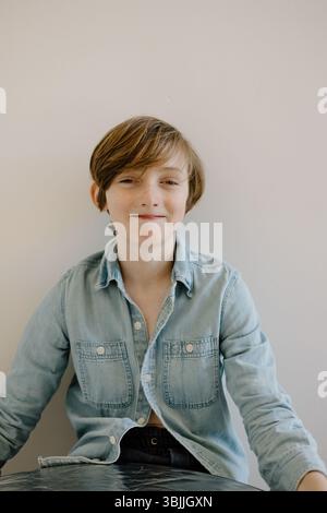 Ragazzo sorridente con camicia in denim su sfondo neutro Foto Stock