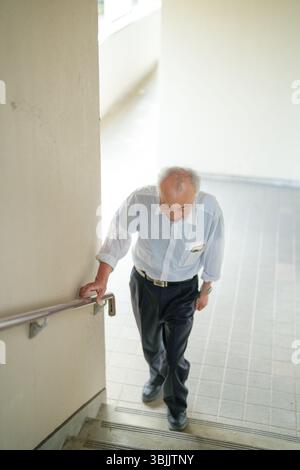 In Giappone, un uomo giapponese alla fine degli anni '70, indossando una camicia bianca, sale le scale di un appartamento usando il corrimano come supporto. Questa tranquilla momen Foto Stock