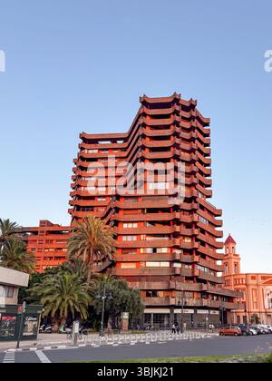 Suggestivo edificio residenziale di colore rosso con audace design geometrico, palme e scena urbana di Valencia, Spagna. Ideale per architettura, viaggi, a. Foto Stock