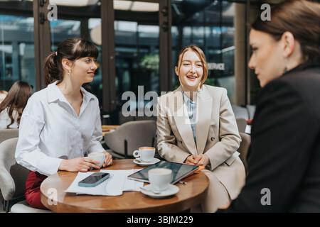 Tre donne d'affari si godono una conversazione amichevole e un caffè durante una riunione informale. Foto Stock