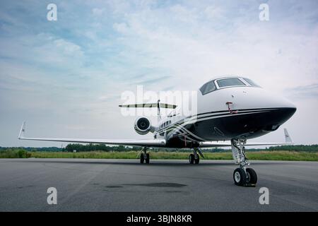 Vista frontale ad angolo basso di un lussuoso jet privato Gulfstream parcheggiato su un asfalto con cielo coperto. L'attrezzatura nasale, la fusoliera e i motori dell'aeromobile sono chiaramente visibili Foto Stock