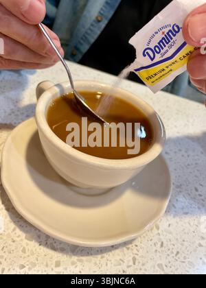 Uomo che aggiunge zucchero al suo caffè mattutino in un ristorante di New York, USA, 2025 Foto Stock