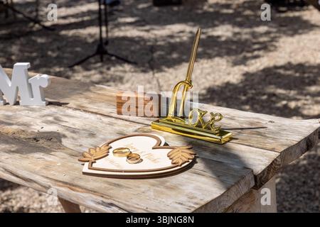 Bellissimo tavolo in legno rustico con fedi nuziali, decorazioni a forma di cuore e una penna dorata per i voti. Foto Stock