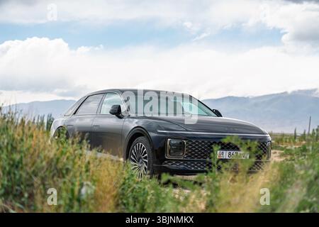 Balykchy, Kirghizistan - 12 maggio 2024: Vista frontale di una grandiosità Hyundai nera 2023 (GN7) parcheggiata tra vegetazione verde e secca con montagne unde Foto Stock