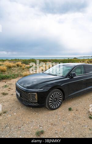 Balykchy, Kirghizistan - 12 maggio 2024: Vista frontale di una Hyundai Grandeur nera 2023 (GN7) parcheggiata su una strada sterrata accanto ad un grande lago blu Foto Stock